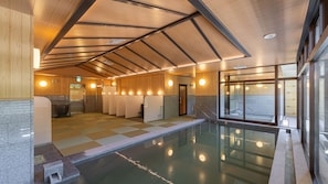 Un espace piscine intérieur moderne, doté d’un sol à carreaux, de murs recouverts de panneaux en bois et d’une paroi vitrée.