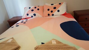 Una cama con un edredón colorido que presenta formas abstractas y lunares, una almohada a juego y una manta marrón.