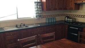 Una cocina con armarios de madera, un lavabo, una estufa y una mesa de comedor con sillas.