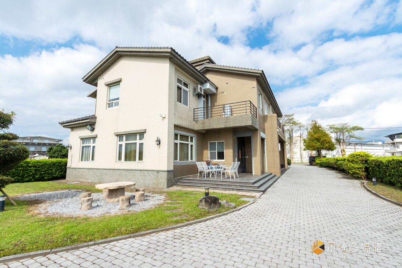 Un edificio residenziale a due piani con un balcone, un vialetto lastricato e un piccolo giardino con tavolo e sedie.