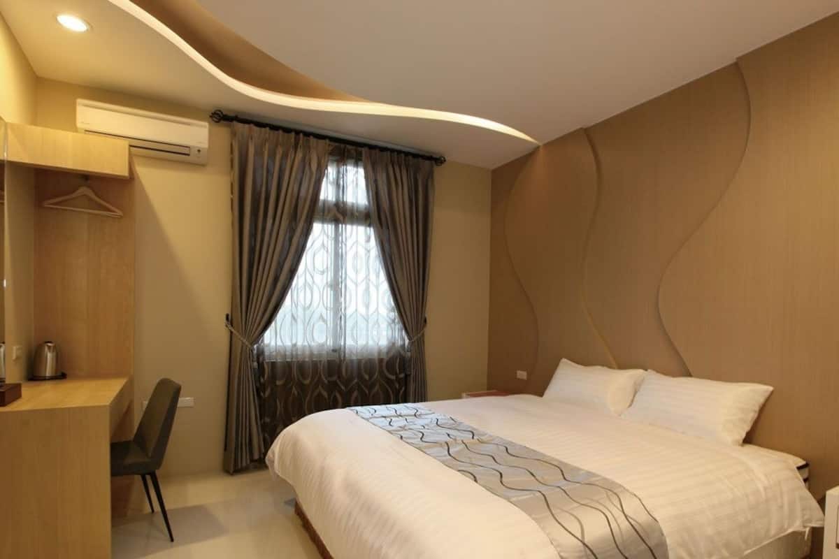 Quarto de hotel moderno com uma cama grande, uma escrivaninha com cadeira, uma TV e um ar condicionado.