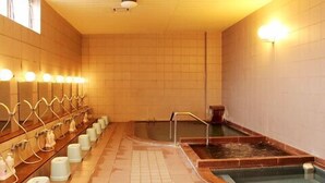 Un área de baños públicos con varias bancas, un jacuzzi central y suelo de baldosas.