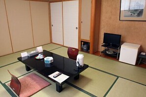 Ein Zimmer mit Tatami-Boden, einem schwarzen Tisch mit Fernbedienung, einem Fernseher und einer kleinen Vitrine.
