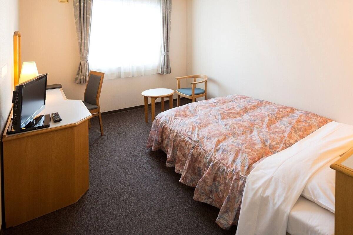 Ett hotellrum med en säng, ett skrivbord med en dator, en stol, ett litet bord och en telefon.