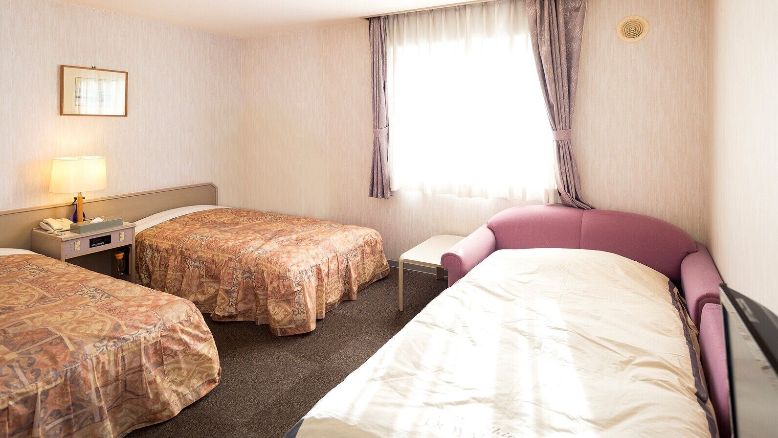 Habitación de hotel con dos camas, una mesita de noche con lámpara y una ventana con cortinas.