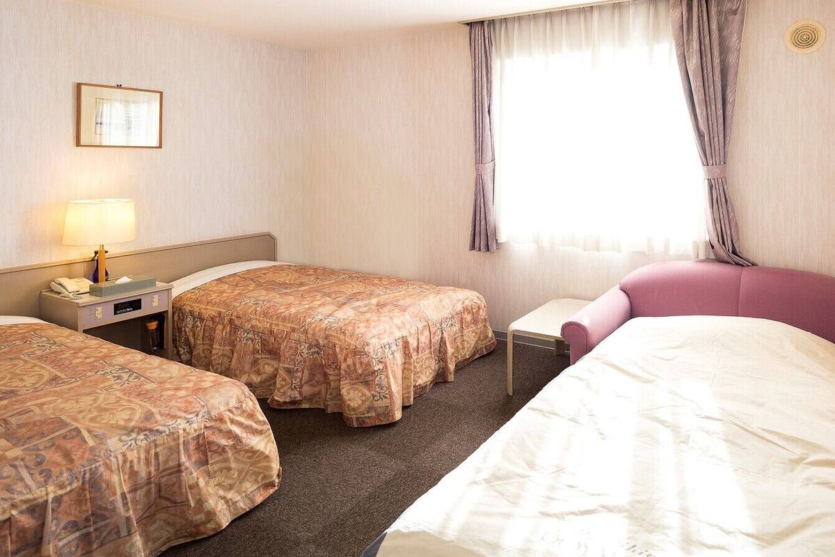 Ett hotellrum med två sängar, ett nattduksbord med en lampa och ett fönster med gardiner.