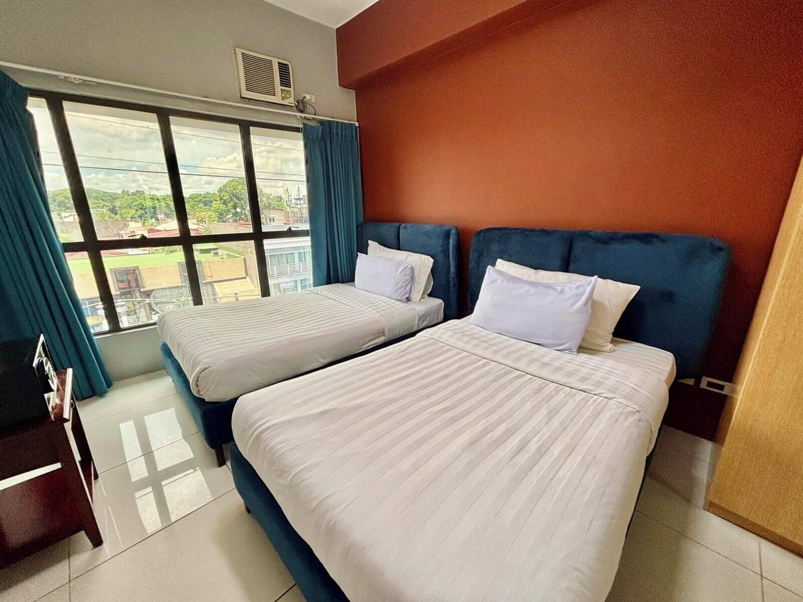 Een hotelkamer met twee bedden, een groot raam met gordijnen en uitzicht op de omgeving.