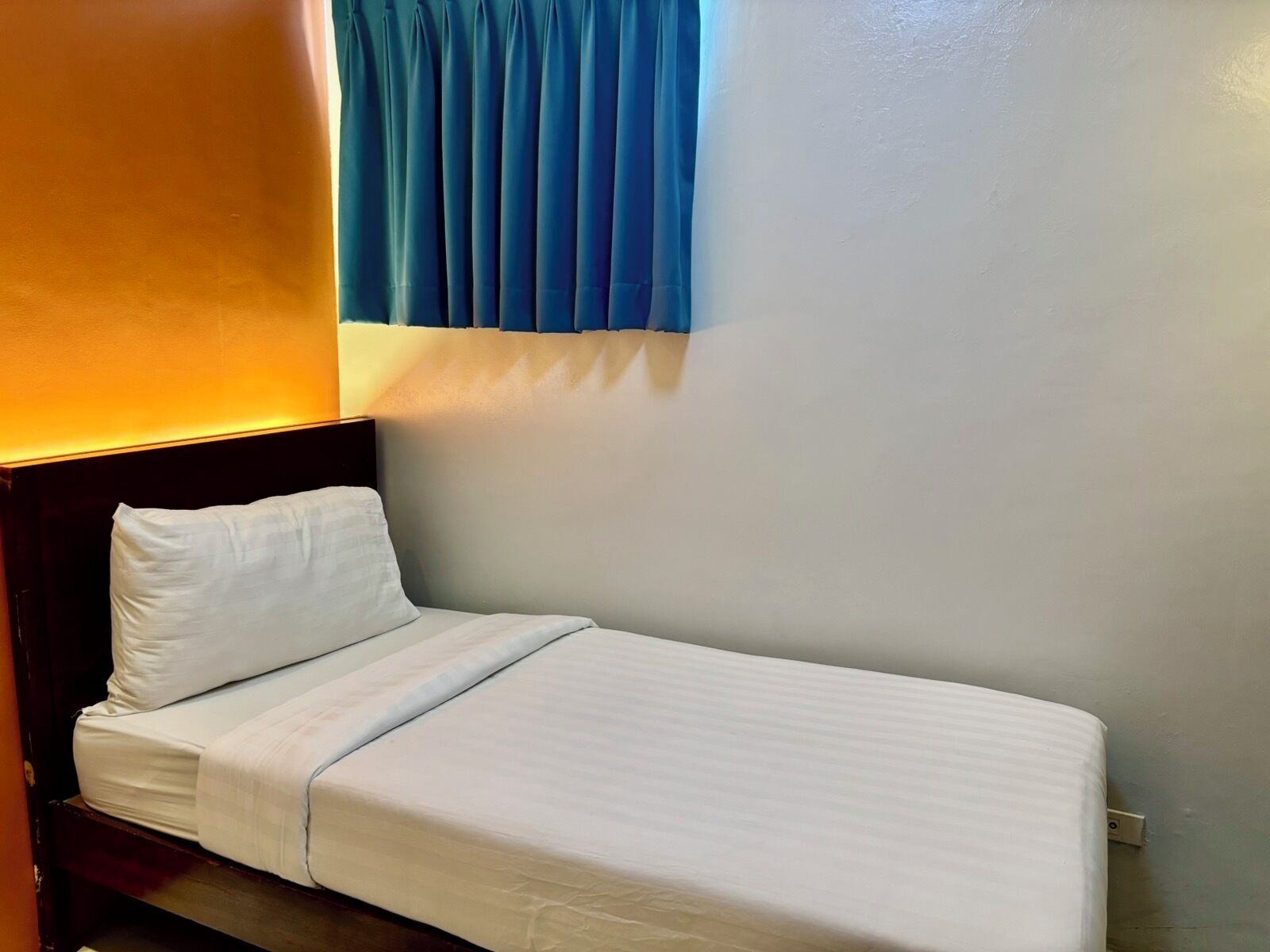 A single bed with white bedding in a room with a dark headboard and a blue curtain.