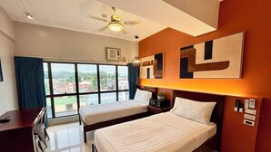 Habitación de hotel con dos camas, un escritorio, un ventilador de techo y un amplio ventanal con vistas.