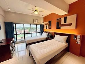 A hotel room with two beds, a desk, a ceiling fan, and a large window with a view. - Pacific Park Hotel (Quezon City)