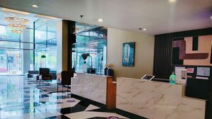 Un vestíbulo de hotel con mostrador de recepción, zona de estar y grandes ventanales con vistas a la calle.