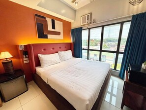 Ein Hotelzimmer mit einem großen Bett, einem Nachttisch, einer Lampe, einer Wand-Klimaanlage und einem mit Vorhängen versehenen Fenster.