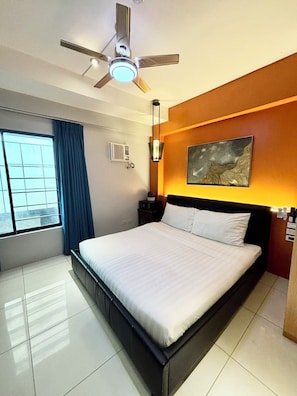 A hotel room with a bed, a ceiling fan, a window with curtains, a wall-mounted air conditioner, and a painting. - Pacific Park Hotel (Quezon City)