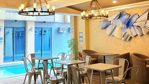 Interior de un restaurante con suelo de madera, sillas y mesas blancas, y vista a una piscina.