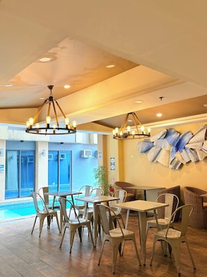 Interior de un restaurante con suelo de madera, sillas y mesas blancas, y vista a una piscina.