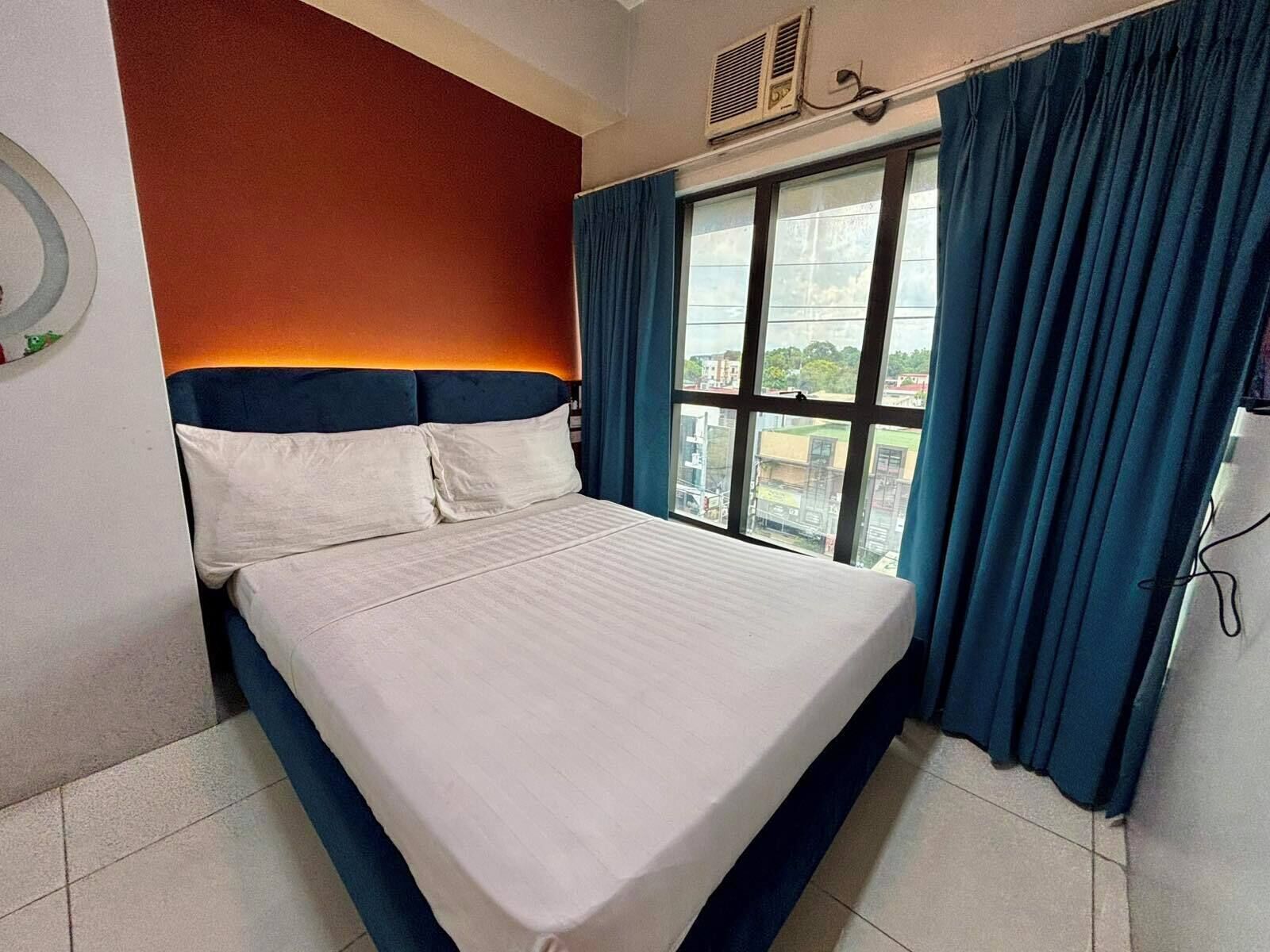 Een hotelkamer met een bed, een raam met gordijnen en een wandairconditioning.