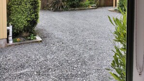 A gravel driveway leading to a house with a view of a hill and a palm tree. - Bay Cottages (Kaikoura)