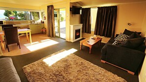 A compact living space with a sofa, a dining table, a kitchen area, and a fireplace. - Bay Cottages (Kaikoura)