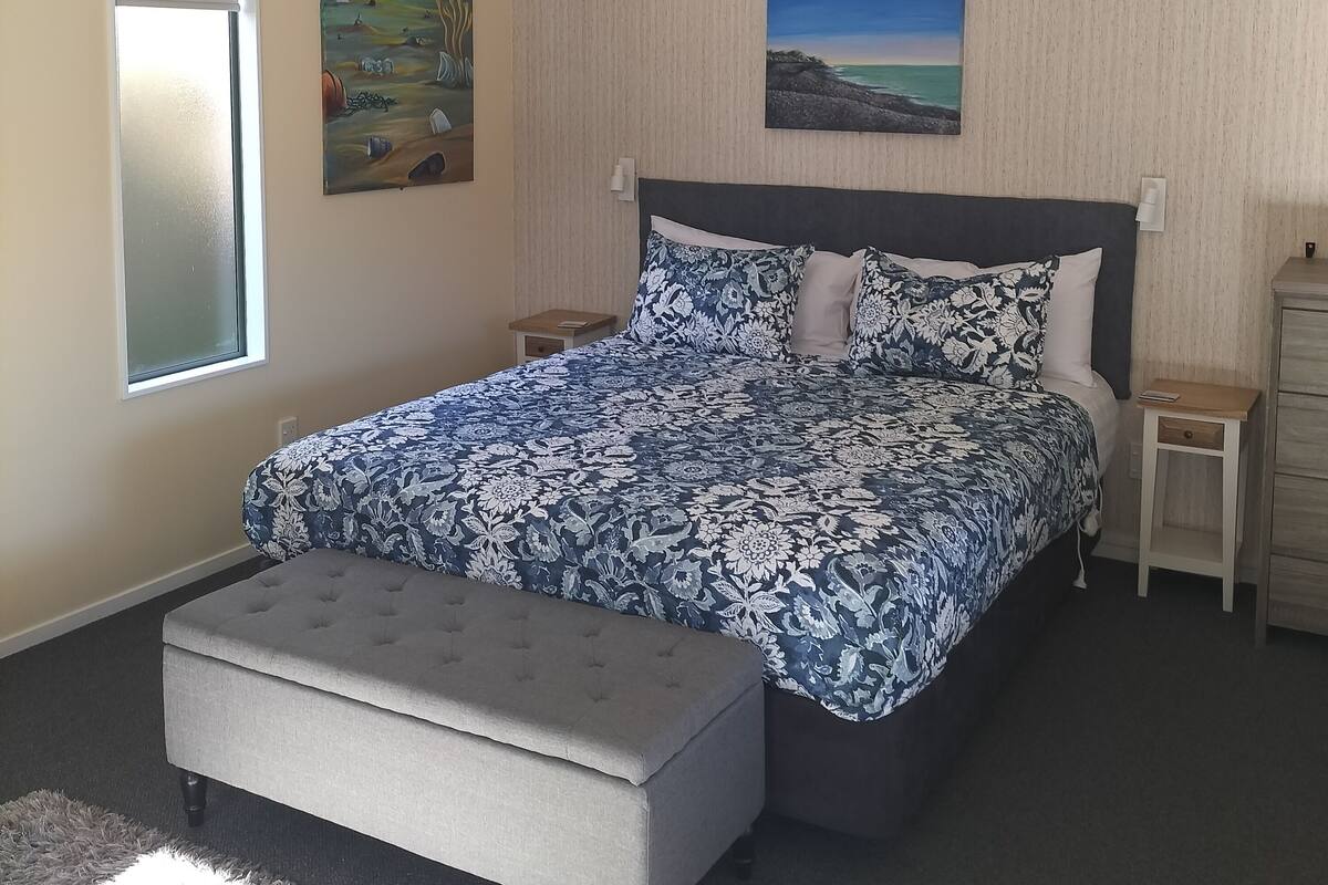 Un dormitorio con cama, mesita de noche, cómoda y dos cuadros en la pared.