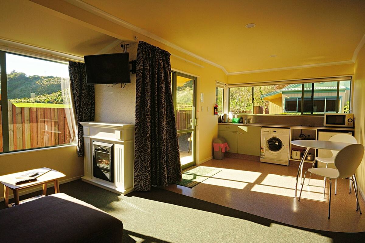Una habitación compacta con chimenea, televisión, zona de cocina con lavadora y mesa de comedor con sillas.
