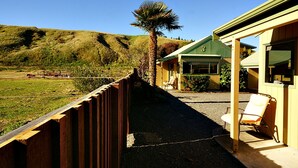 A wooden deck with a view of a hill and a building with a green roof. - Bay Cottages (Kaikoura)
