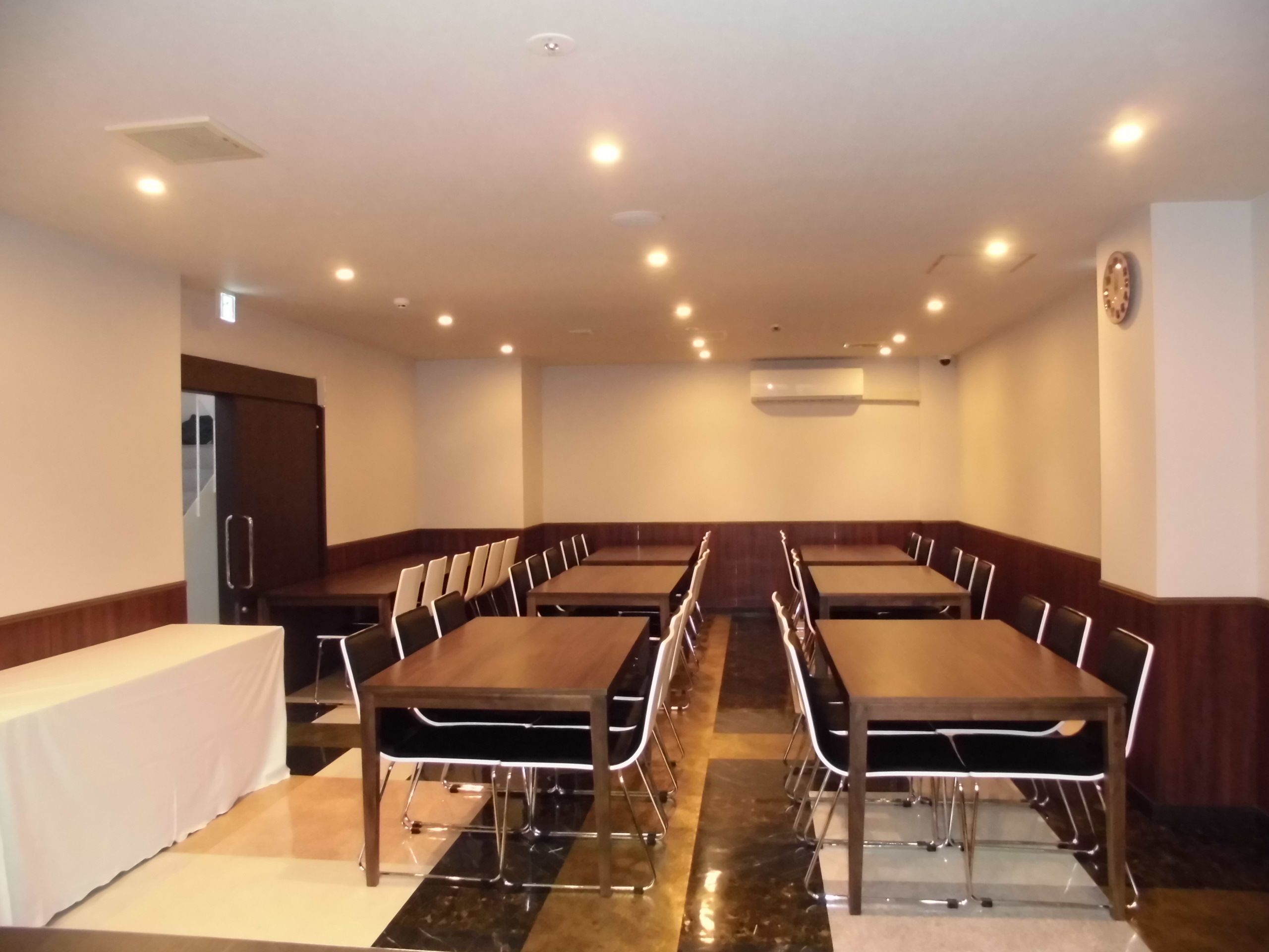 A conference room with a long table and chairs, recessed ceiling lights, and an air conditioning unit on the wall.