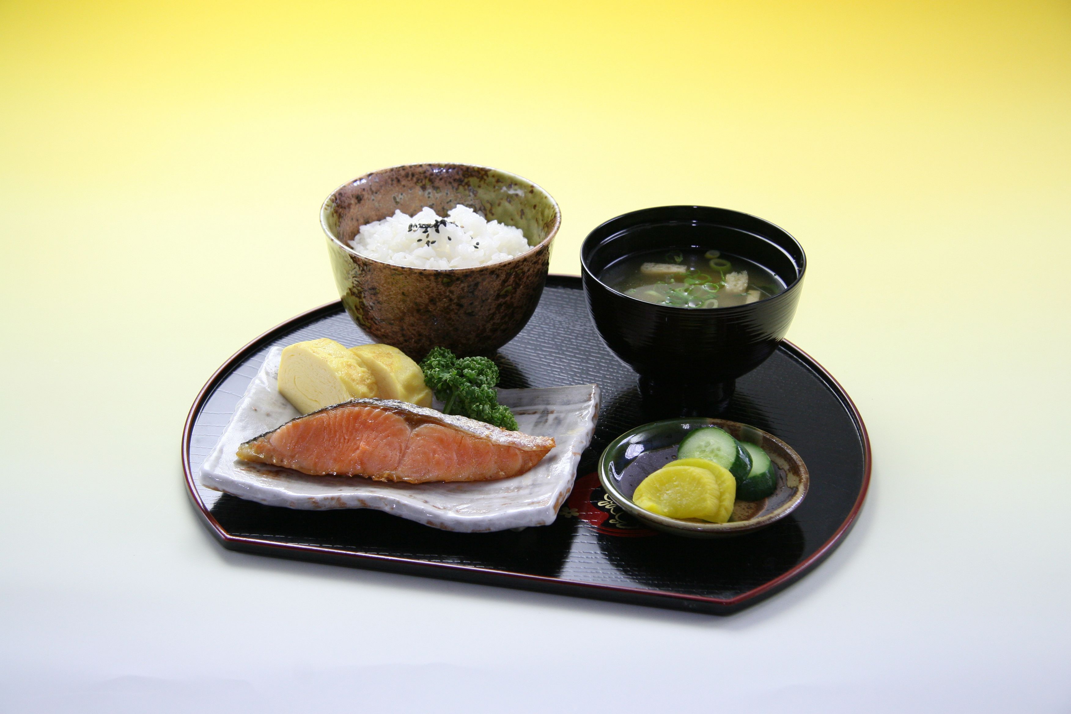 Ein Tablett mit Lachs, Reis, Suppe und einer kleinen Schale eingelegtes Gemüse.