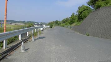 Une route asphaltée bordée de glissières métalliques et de cônes de signalisation, entourée de verdure et sous un ciel dégagé.