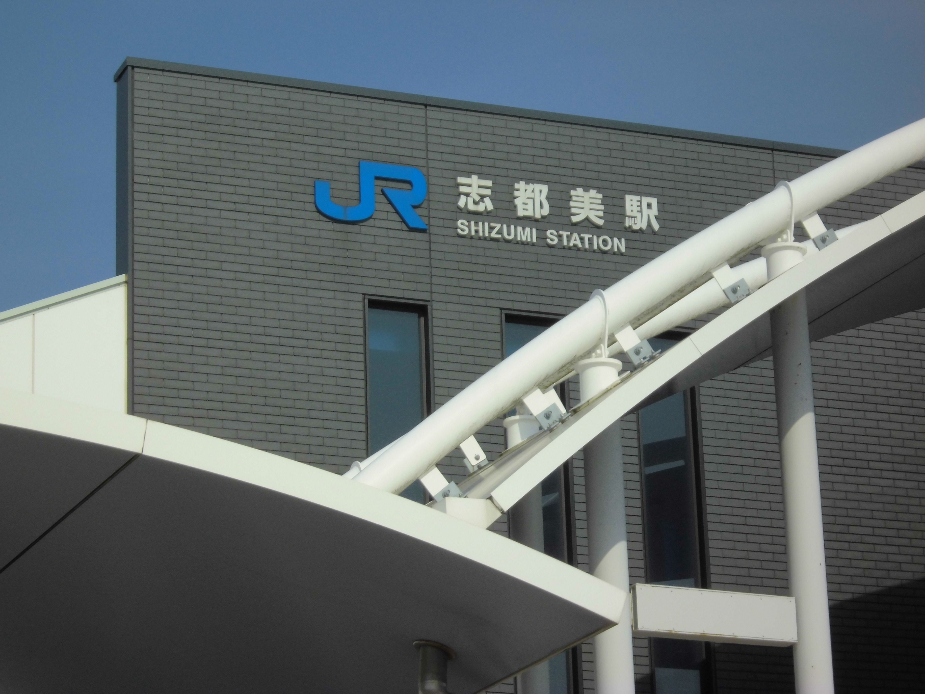 A building with a sign that reads "SHIZUMI STATION" and a logo with the letter "J".