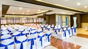 A spacious hall with rows of chairs covered in white and blue sashes, a stage with curtains, and a modern ceiling design. - Octave Hotel & Spa JP Nagar (Bengaluru)