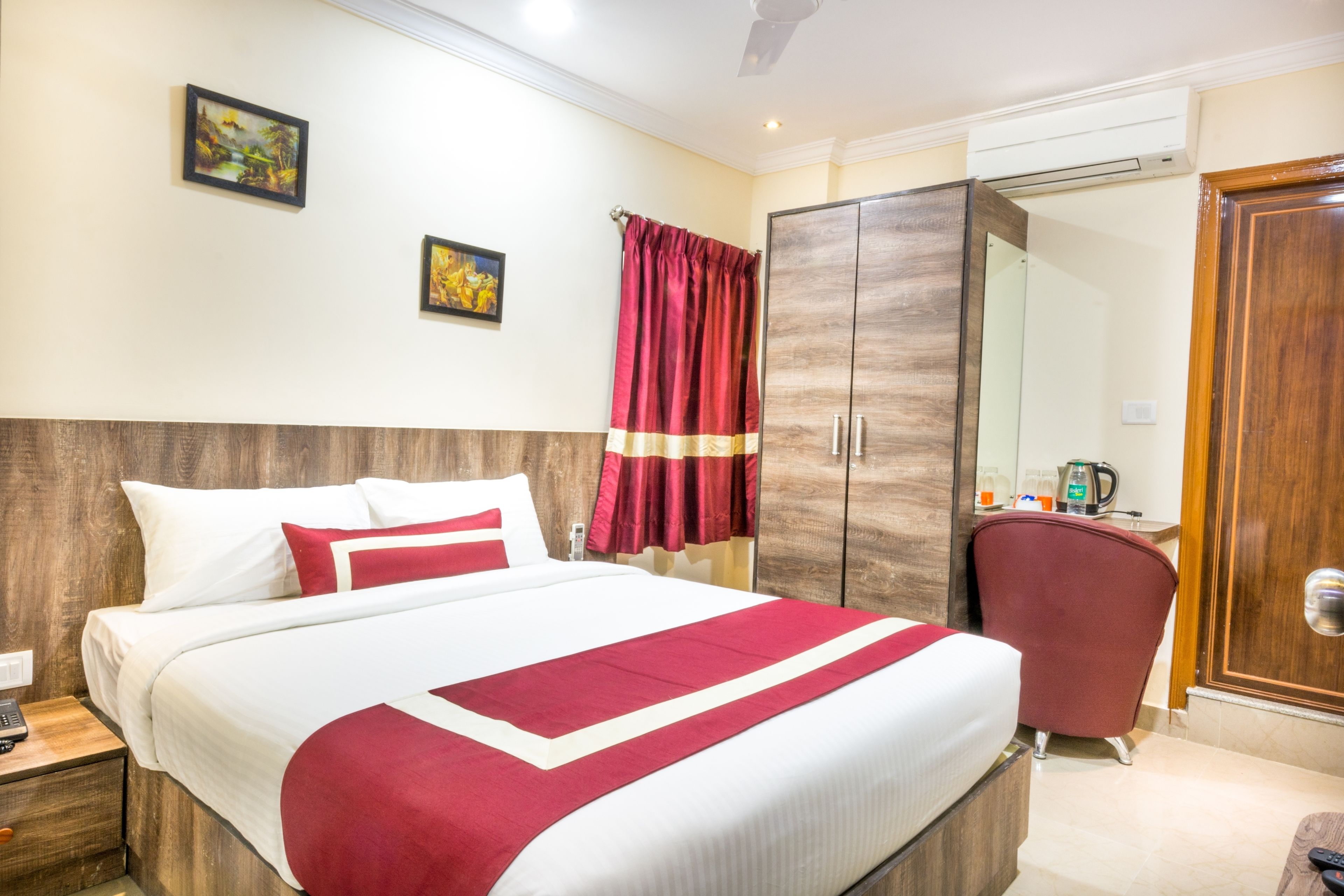 A hotel room with a large bed, a wardrobe, a desk with a chair, and two framed pictures on the wall.