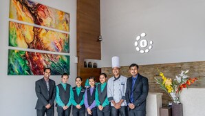 A group of people standing in a modern lobby with abstract paintings on the wall and a logo above the reception desk. - Octave Hotel & Spa JP Nagar (Bengaluru)