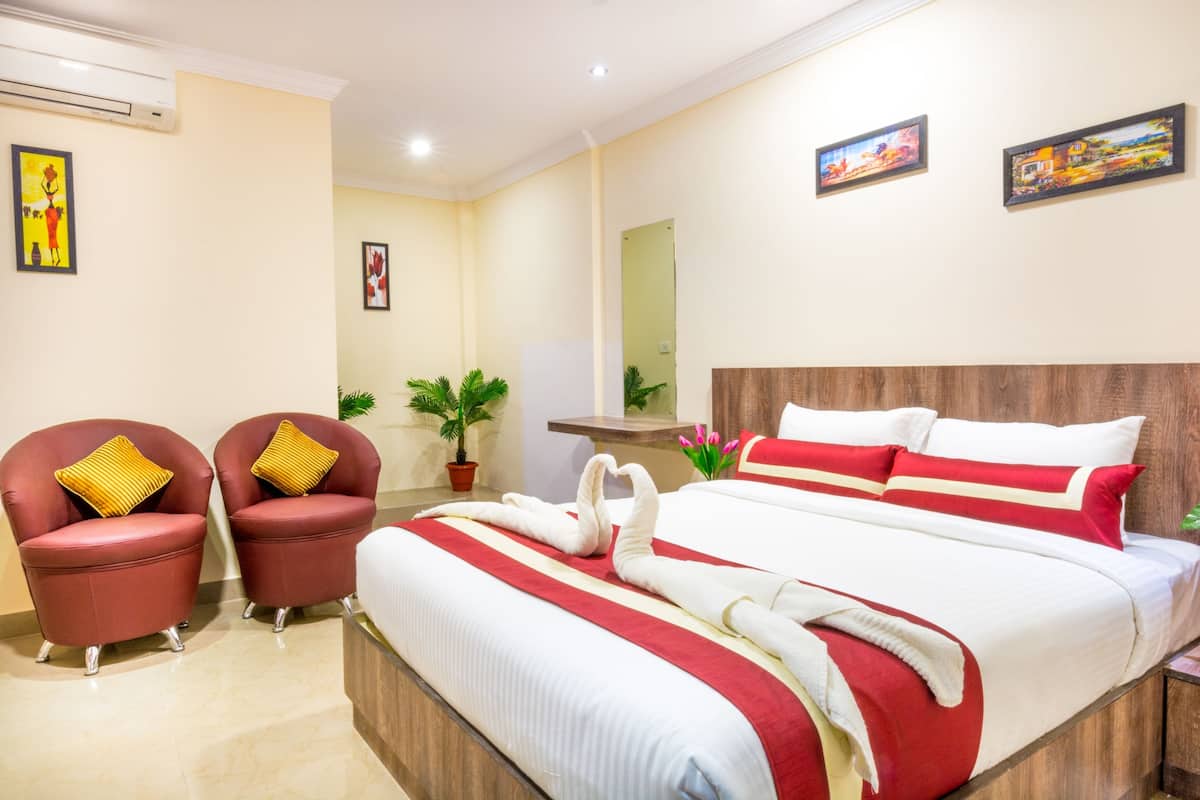 A hotel room with a large bed, two red armchairs, a wooden headboard, and artwork on the walls.