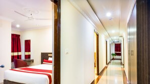A hotel room with a bed, a desk, and a chair. There is a hallway with a plant and a door at the end. - Octave Hotel & Spa JP Nagar (Bengaluru)