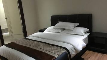 A neatly made bed with white linens and a patterned throw blanket, a dark headboard, and a small bedside table with a lamp.
