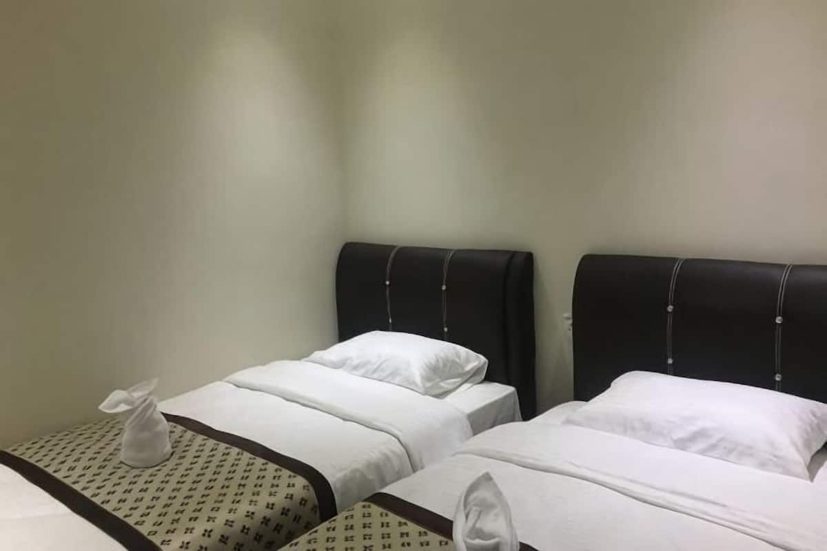 Duas camas de solteiro com cabeceiras, roupa de cama branca e um edredom estampado na cama da esquerda.