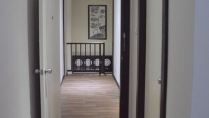 A hallway with wooden flooring, a black-framed door on the right, and a white door on the left. There is a framed artwork on the wall and a black railing in the background. - Qu Lin Resident (Sibu)
