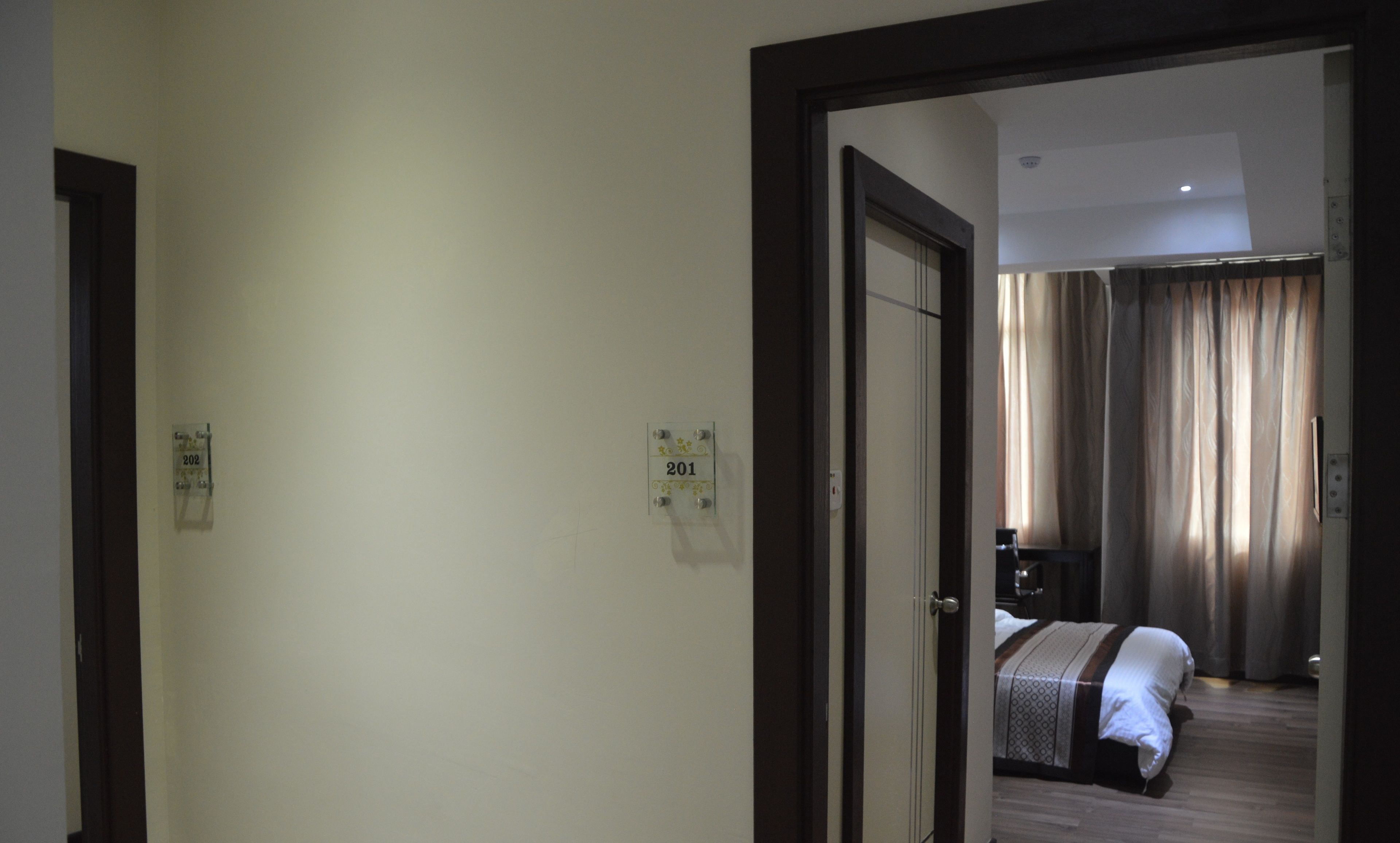 Quarto de hotel com cama, escrivaninha e janela com cortinas. Dois números de porta na parede.