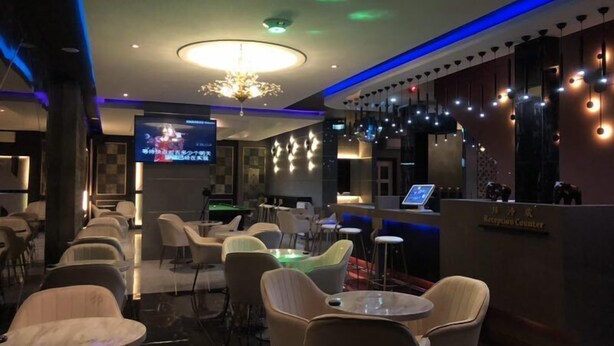 A modern reception area with a reception counter, seating area with chairs and tables, a television screen, and ambient lighting. - Qu Lin Resident (Sibu)