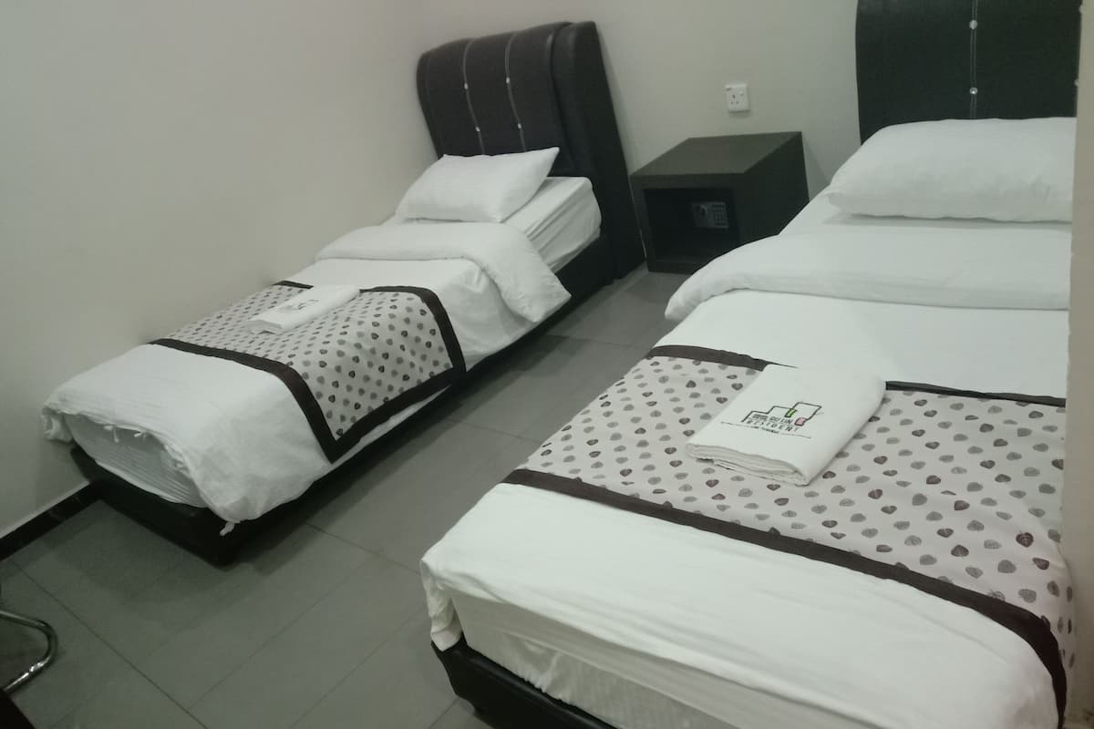 Quarto de hotel com duas camas de solteiro, cada uma com colcha branca e cabeceira marrom. Há uma pequena mesa entre as camas e uma tomada na parede.