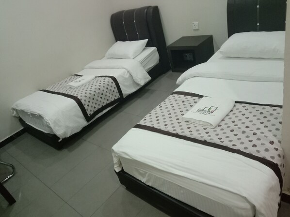 A hotel room with two single beds, each with a white bedspread and a brown headboard. There is a small table between the beds, and a power outlet on the wall.