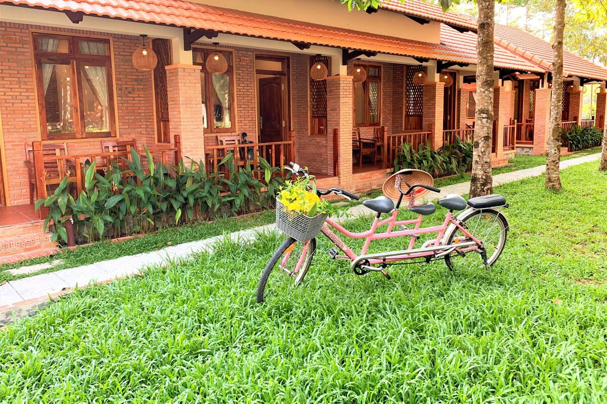 A brick building with a tiled roof, a bicycle with a basket of flowers, and a well-maintained lawn.