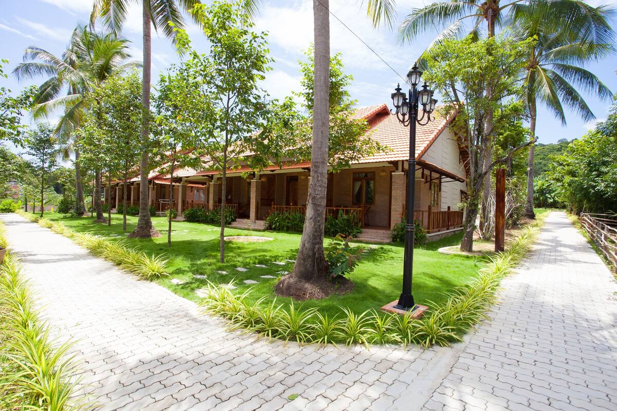 A house with a tiled roof, surrounded by palm trees and a paved pathway.