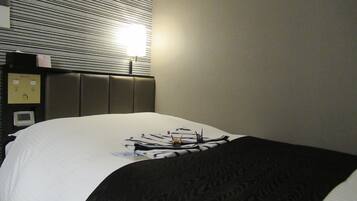 A hotel room with a bed, a headboard, a wall-mounted clock, and a window with blinds.