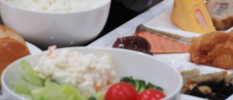A variety of dishes including rice, a salad with lettuce and cherry tomatoes, and a plate with a piece of meat and a slice of yellow fruit.