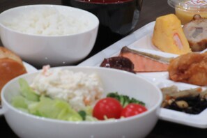 Variedad de platos que incluyen arroz, una ensalada con lechuga y tomates cherry, y un plato con un trozo de carne y una porción de fruta amarilla.