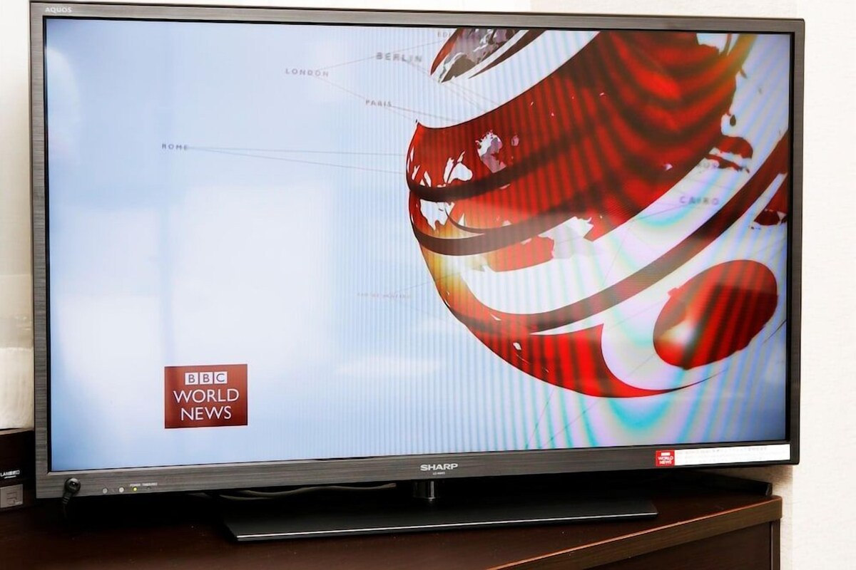A flat-screen TV displaying the BBC World News logo, mounted on a wooden stand.