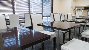 Una sala de conferencias con una gran mesa y sillas, una máquina de café y un ventanal con persianas.