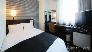 Una habitación de hotel con cama, televisor, escritorio y ventana con cortinas.