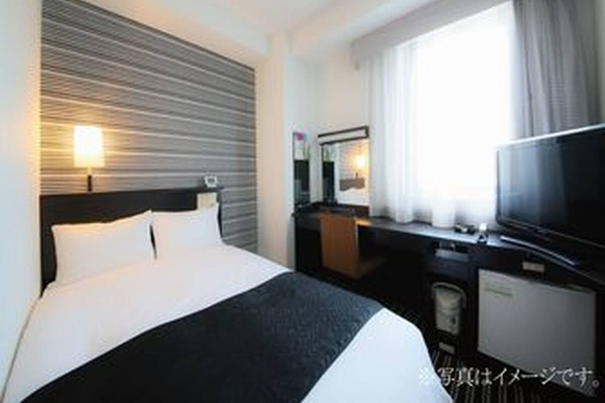 A hotel room with a bed, a television, a desk, and a window with curtains.